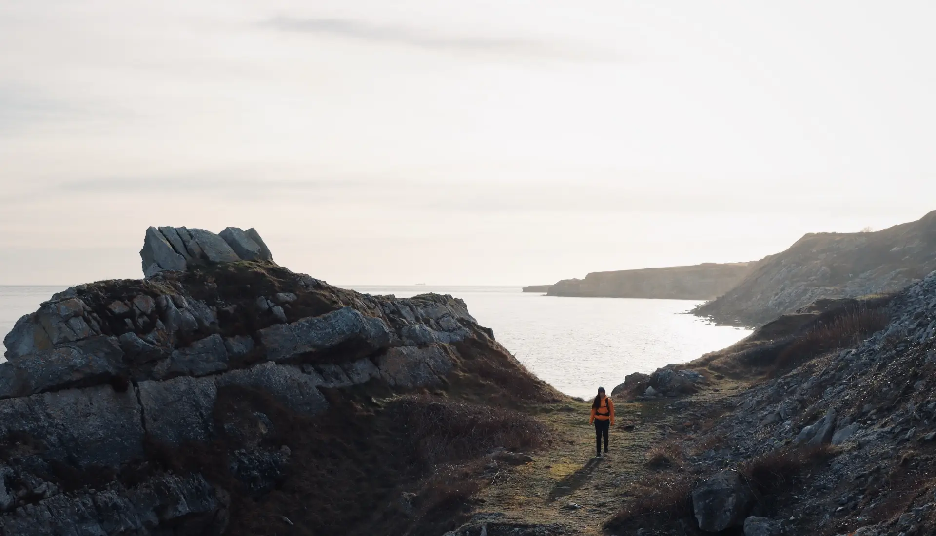 Woman in hiking gear walking along a rocky coastline